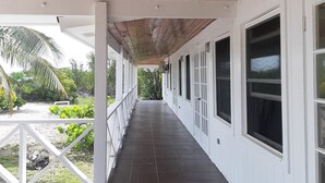 Un pasillo cubierto con techo de madera, paredes blancas y ventanas amplias.