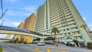 A high-rise hotel with multiple balconies, a pedestrian bridge, and a clear sky.