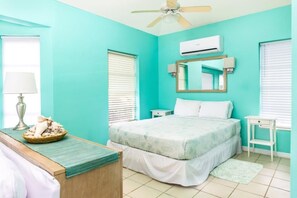 A bedroom with a bed, a bedside table, a lamp, a mirror, and an air conditioning unit.