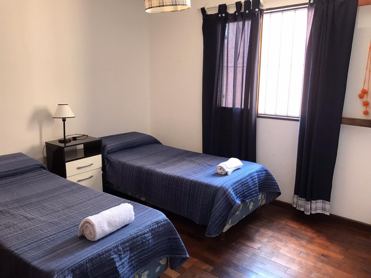 A room with two beds, a nightstand, a lamp, and a window with curtains.