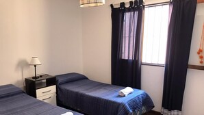 A room with two beds, a nightstand, a lamp, and a window with curtains. - Departamento Sarmiento Salta (Salta)