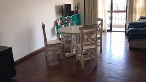 A dining area with a round wooden table and chairs, a television on a teal stand, and a sliding glass door leading to an outdoor area. - Departamento Sarmiento Salta (Salta)