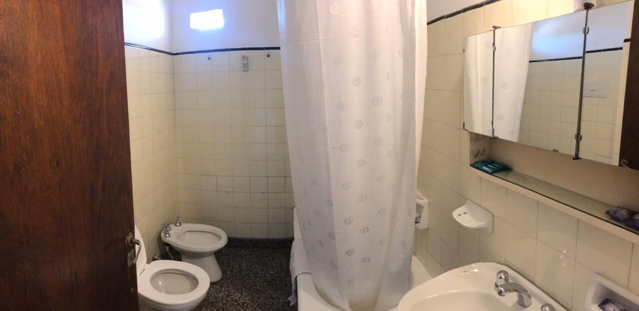 A bathroom with two toilets, a sink, a mirror, and a shower curtain.
