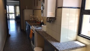 A narrow kitchen with a granite countertop, a built-in oven, and a refrigerator. - Departamento Sarmiento Salta (Salta)