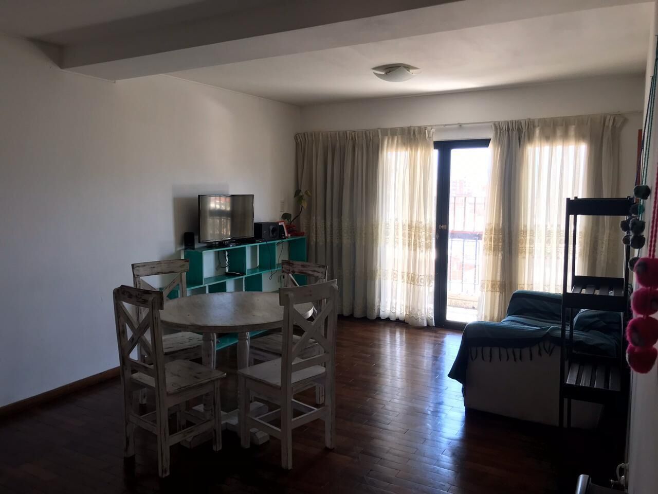 A room with a dining table and chairs, a bunk bed, a TV, and a window with curtains.