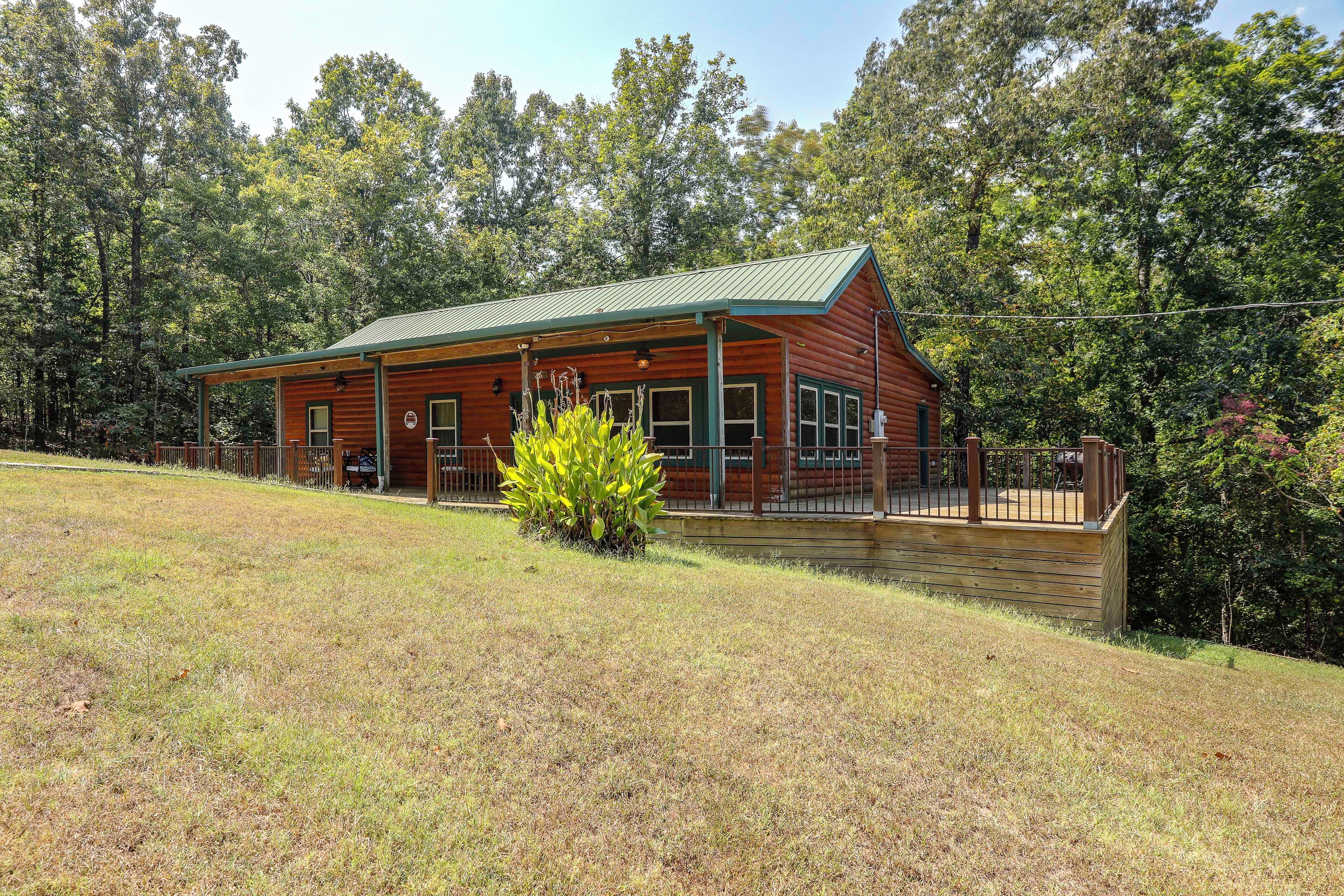 A log cabin with a green roof, a porch, and a small garden in front.