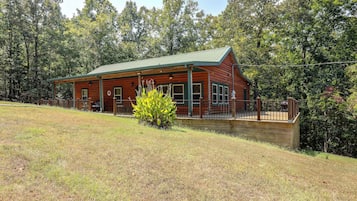 A log cabin with a green roof, a porch, and a small garden in front.