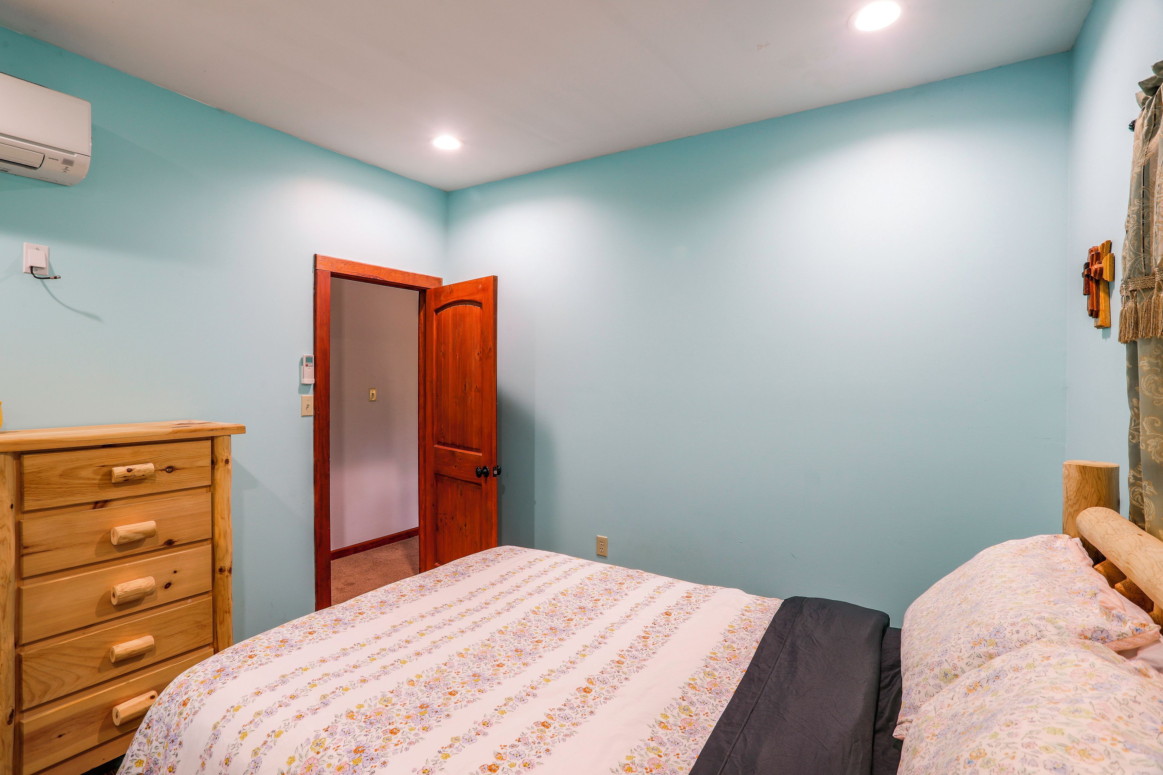 A bedroom with a wooden dresser, a bed with floral bedding, a wooden door, and a light blue wall.