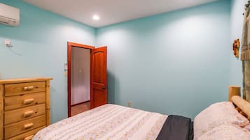 A bedroom with a wooden dresser, a bed with floral bedding, a wooden door, and a light blue wall.