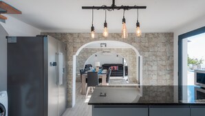 Une cuisine moderne avec un mur de crédence en pierre, un coin repas avec un canapé et une table, et une vue sur l’extérieur.