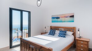 Une chambre à coucher avec un lit en bois, une table de chevet, une commode et un tableau représentant un coucher de soleil sur l’eau.