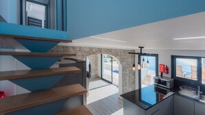 Une cuisine moderne avec un îlot central, un escalier avec des marches en bois et un mur en pierre.