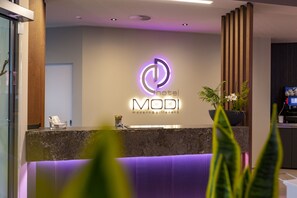 A hotel reception desk with a modern design, featuring a neon sign and a potted plant.