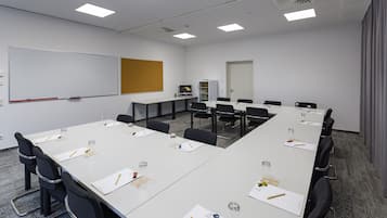 Un salón de conferencias con una larga mesa, sillas, una pizarra y una pantalla de proyector.