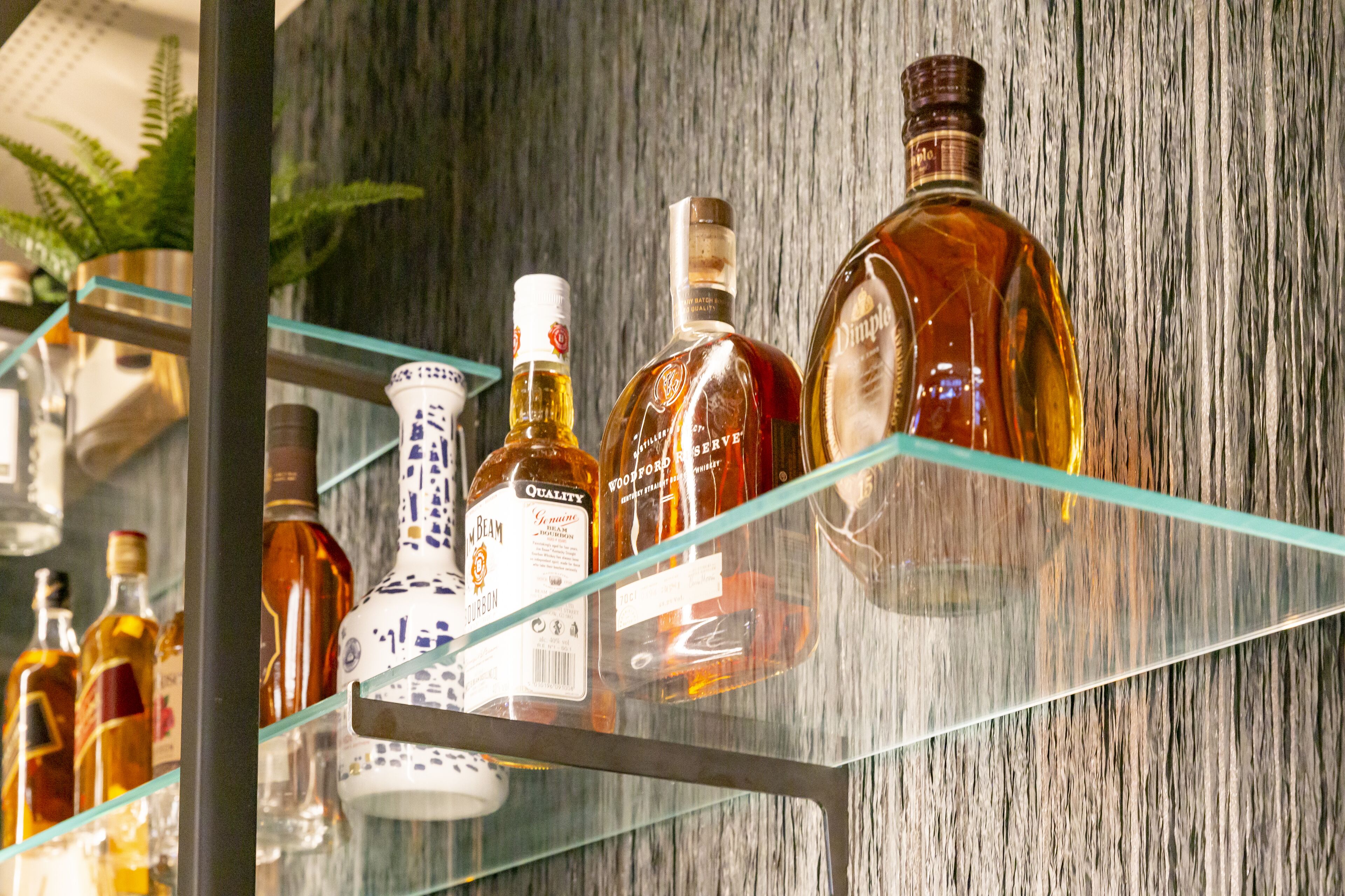Una repisa de vidrio con varias botellas de licor frente a una pared de madera.