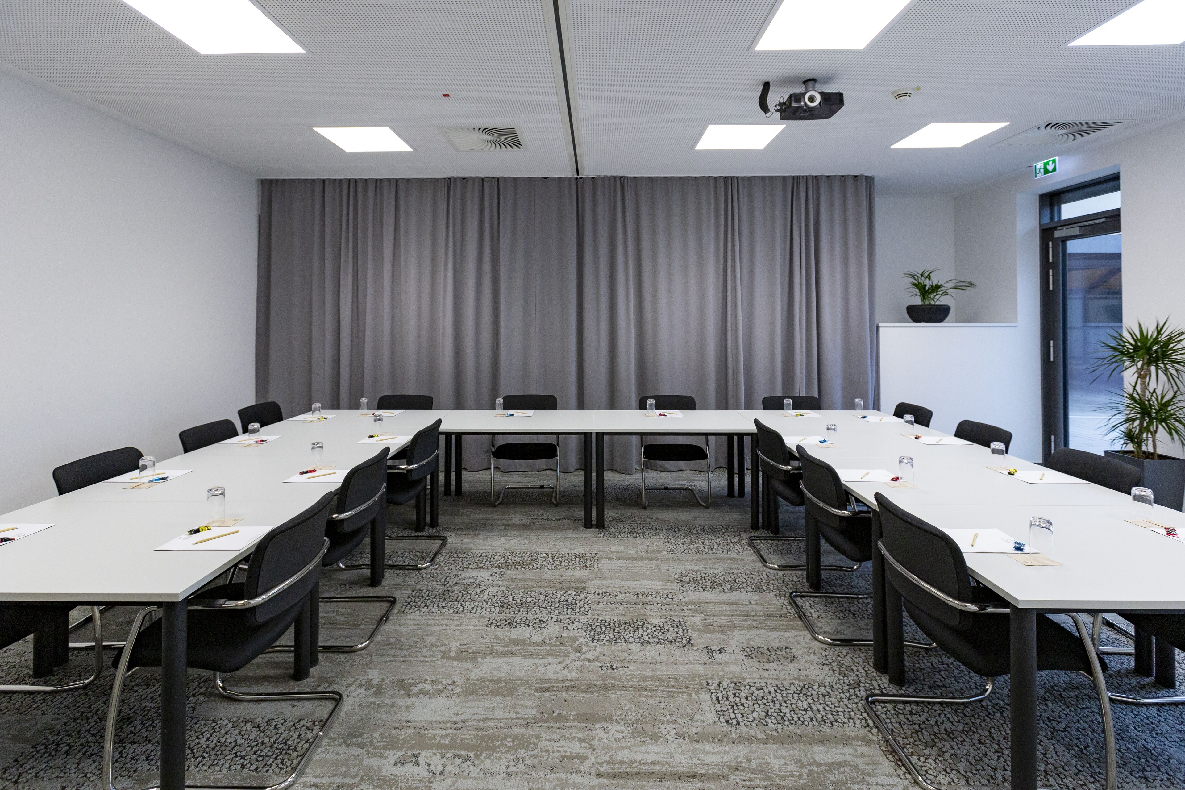 Una sala de conferencias con una mesa larga, sillas, un proyector y una cortina.