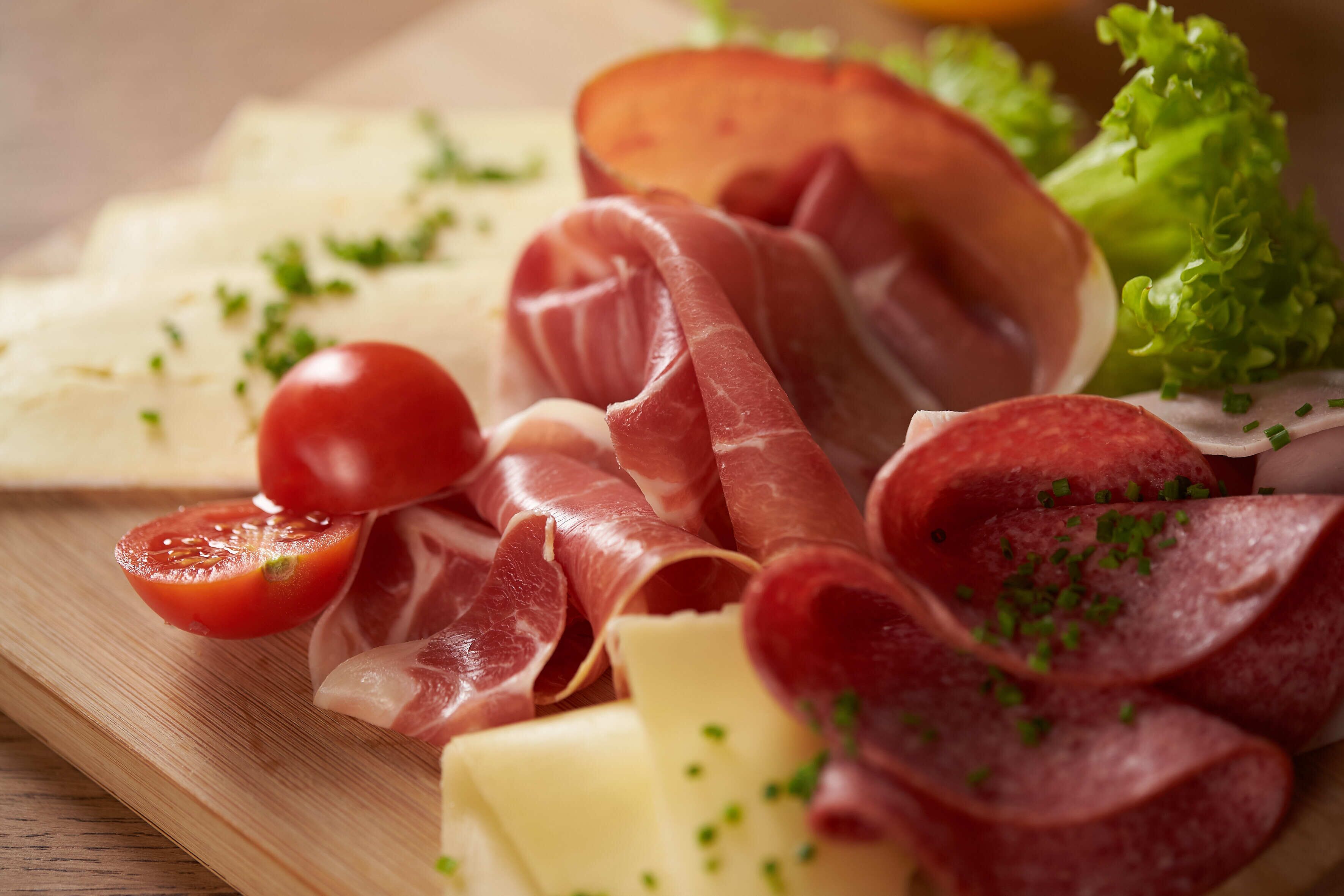 Ein Holzbrett mit verschiedenen Wurstwaren, Käse und einer Kirschtomate.