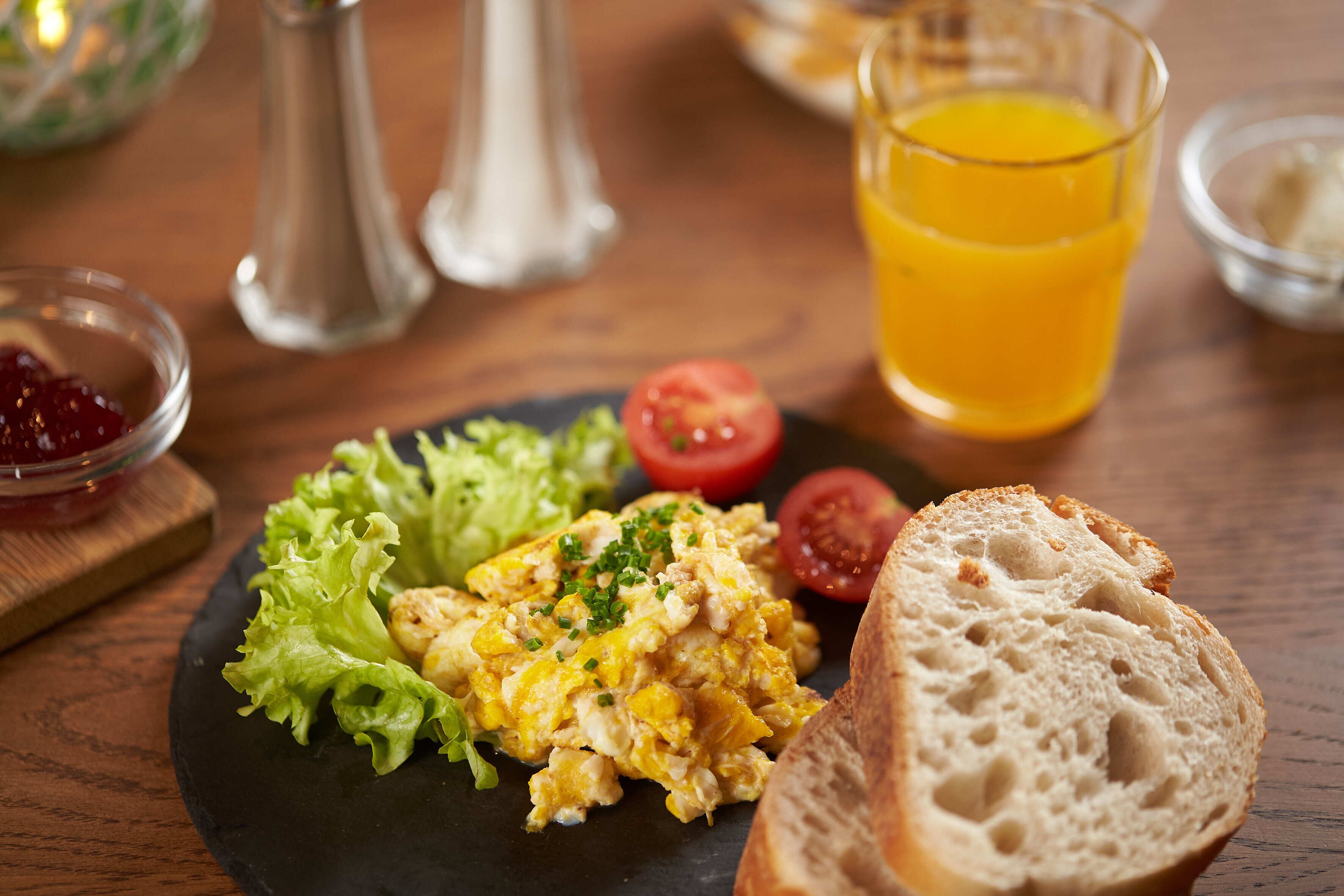 Un plato de desayuno con huevos revueltos, tostadas, lechuga y un vaso de jugo de naranja.