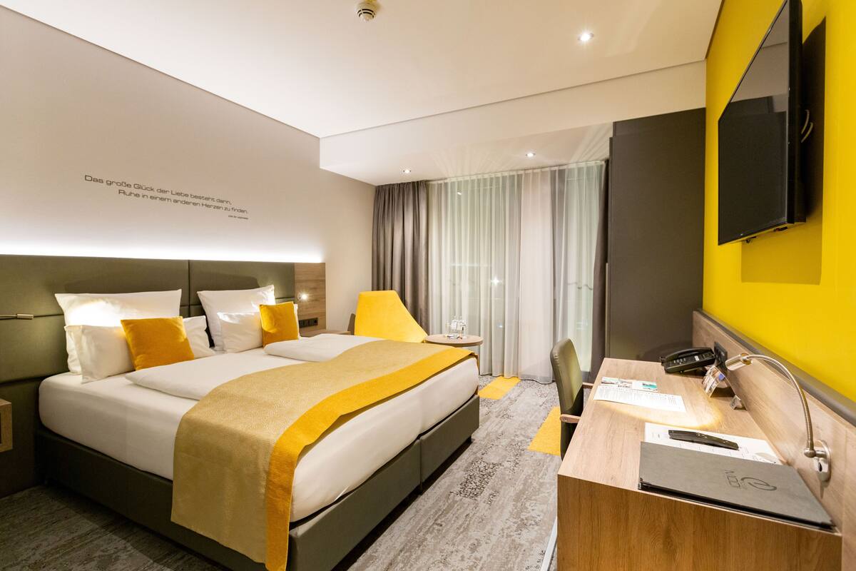 Una habitación de hotel moderna con una cama grande, una mesita de noche y un escritorio con una computadora portátil.