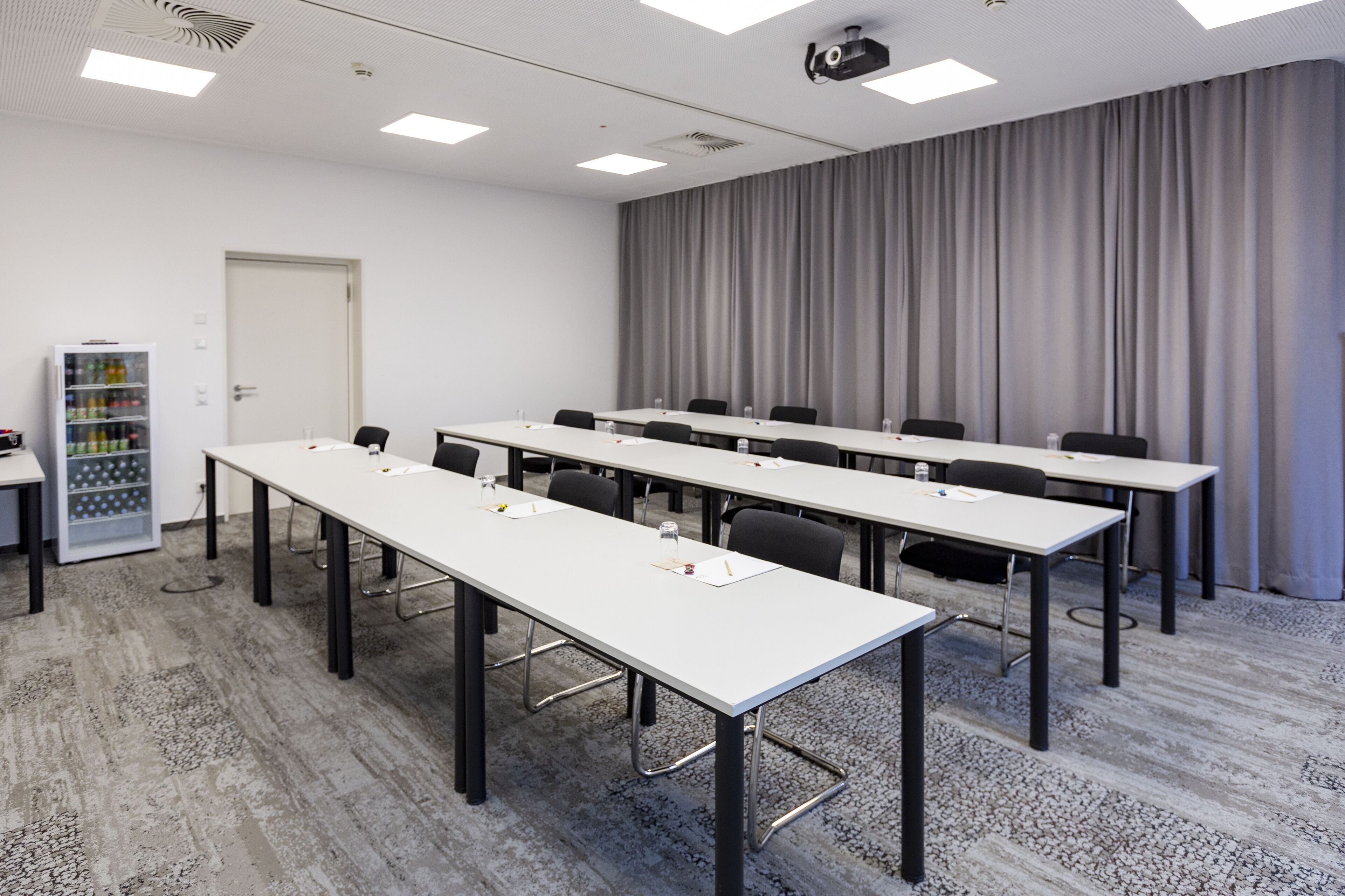 A conference room with long tables, chairs, a projector, and a curtain backdrop.