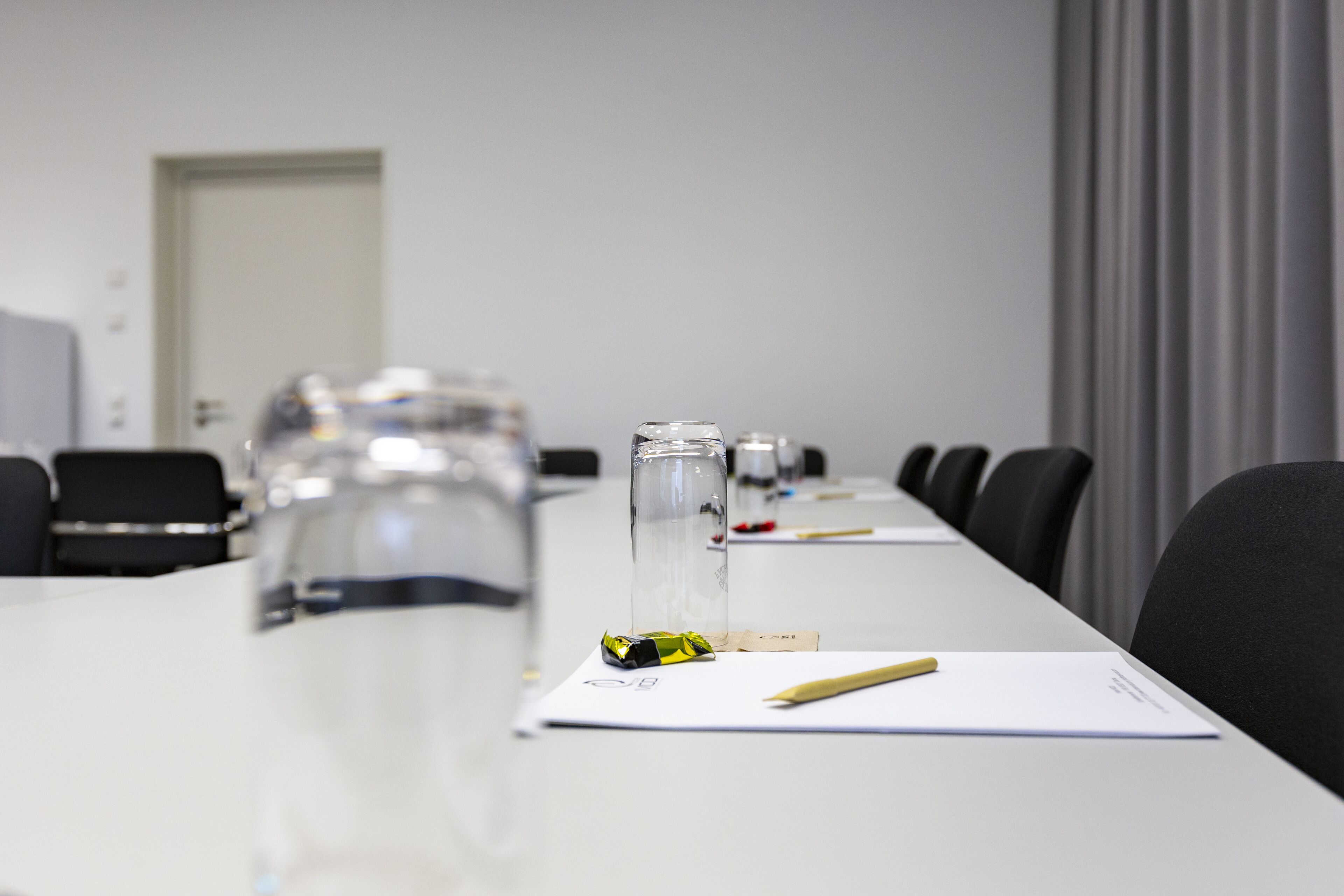 A conference room with a long table, chairs, a water dispenser, a glass, a notebook, and a pen.