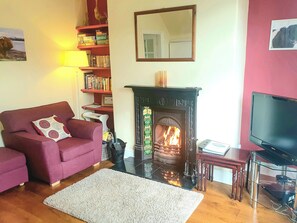 A cozy living room with a fireplace, a sofa, a television, and a bookshelf.