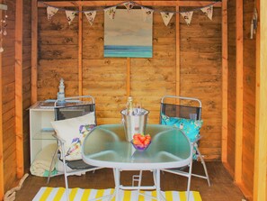 A cozy wooden cabin with a small dining area featuring a glass table, metal chairs, and a bottle of champagne. - 2 bedroom accommodation in Creetown, near Newton Stewart (Creetown, near Newton Stewart)