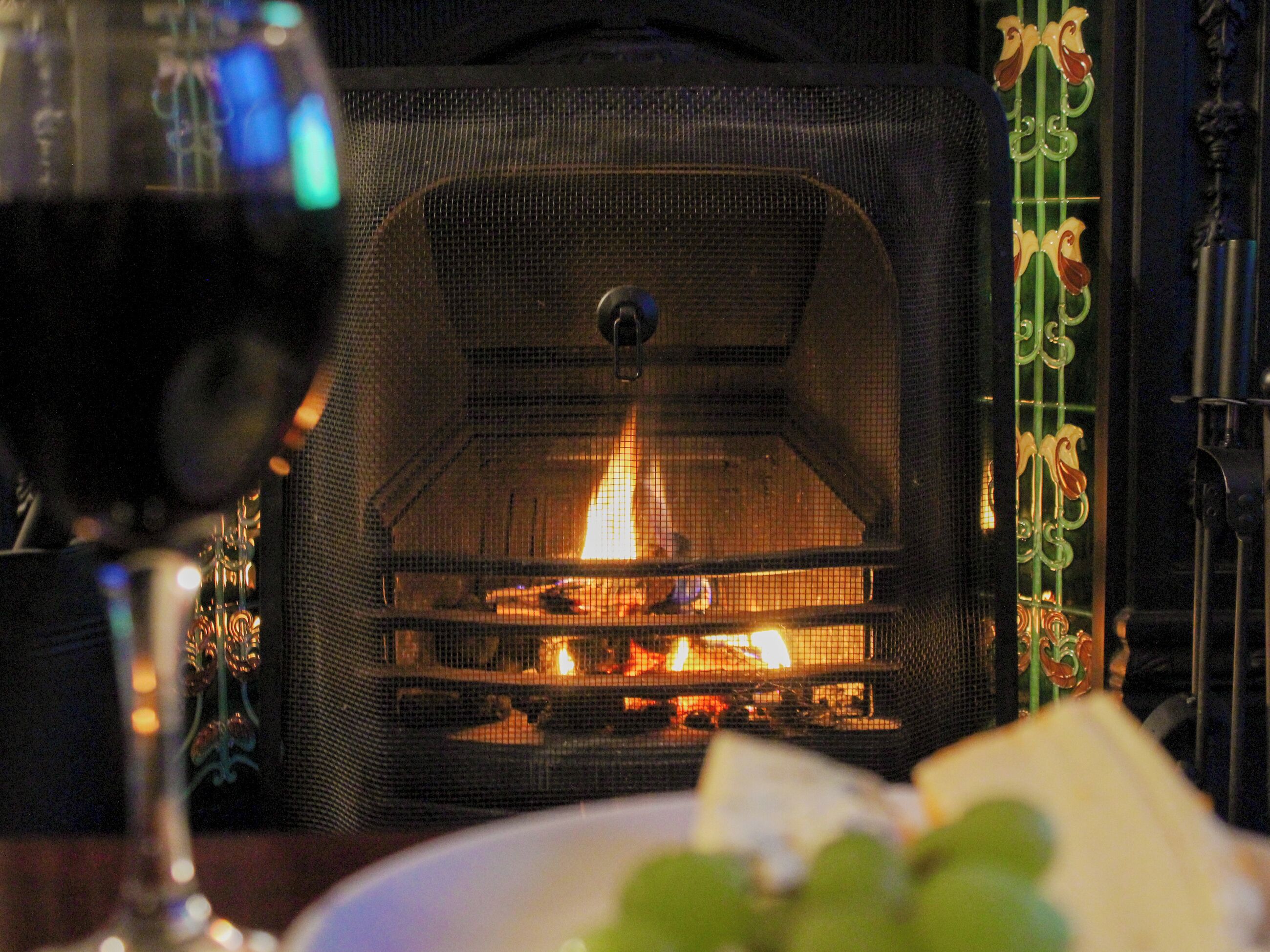 Una chimenea con fuego visible, una copa de vino tinto y elementos decorativos a su alrededor.
