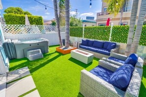 Un jardin avec une pelouse artificielle, un jacuzzi, un ensemble de meubles de salon et un espace barbecue.