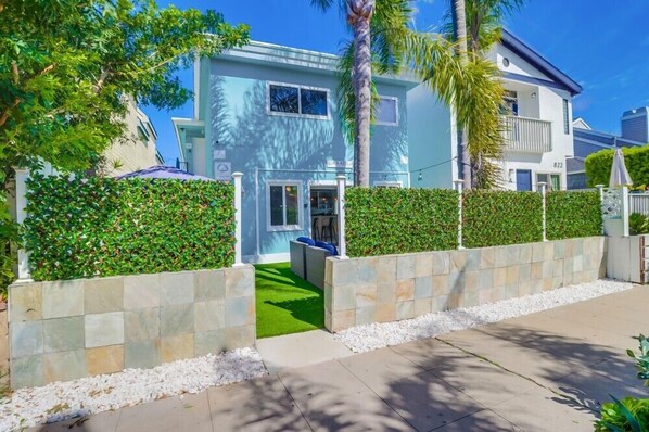 Une maison moderne à deux étages, à la façade bleu clair, avec un chemin en pierre et une pelouse bien entretenue.