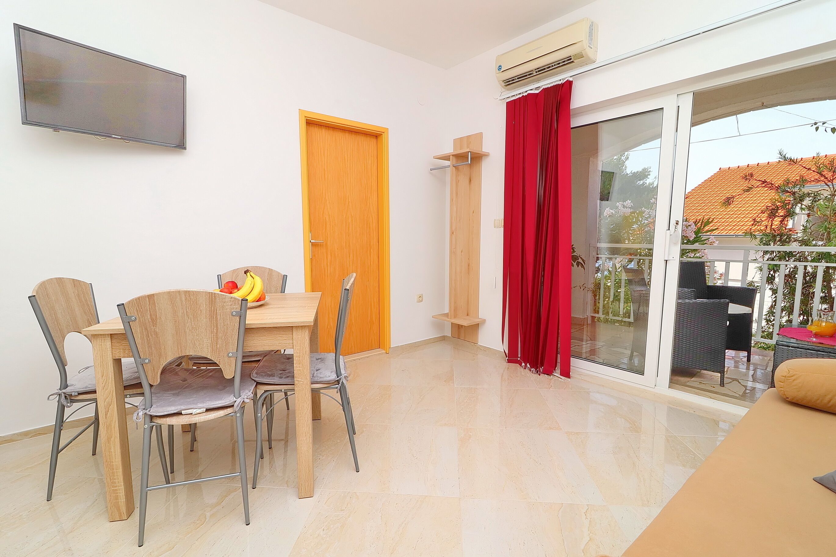 A dining area with a table and chairs, a TV mounted on the wall, and a sliding glass door leading to an outdoor balcony.