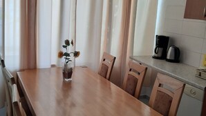 Ein Essbereich mit Holztisch und -stühlen, einer Vase mit Blumen und einer Küchenzeile mit Kaffeemaschine.
