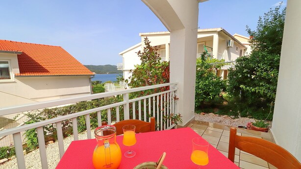 Ein Balkon mit rotem Tischleinentuch, zwei Stühlen, einer Kanne Orangensaft und einer Schale mit Löffel.