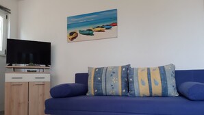 Ein Zimmer mit einem blauen Sofa, einem Fernseher auf einer Holzkommode und einem Bild von Kajaks an der Wand.