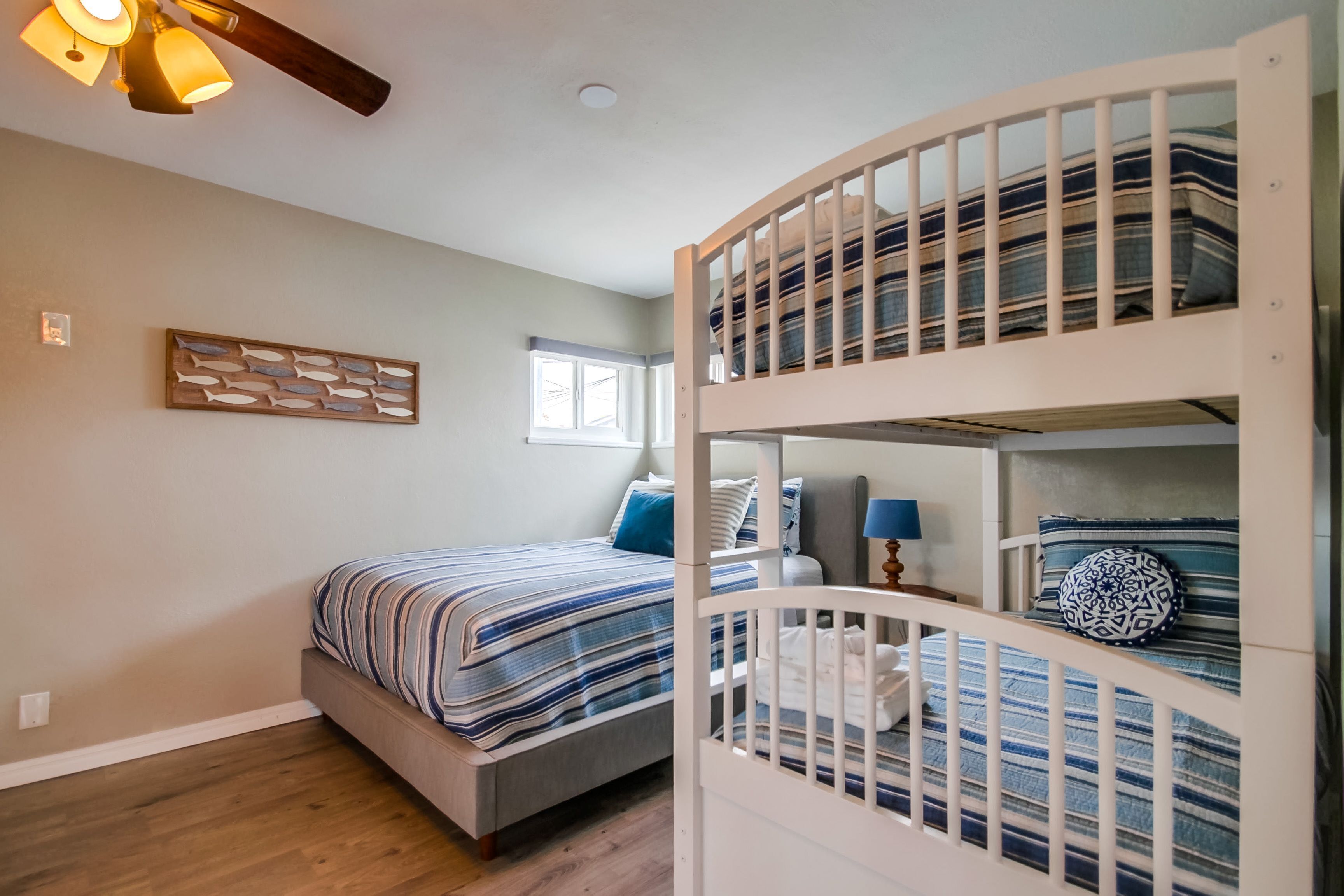 A bedroom with a bunk bed, a single bed, a ceiling fan, a window, and a wall-mounted light fixture.