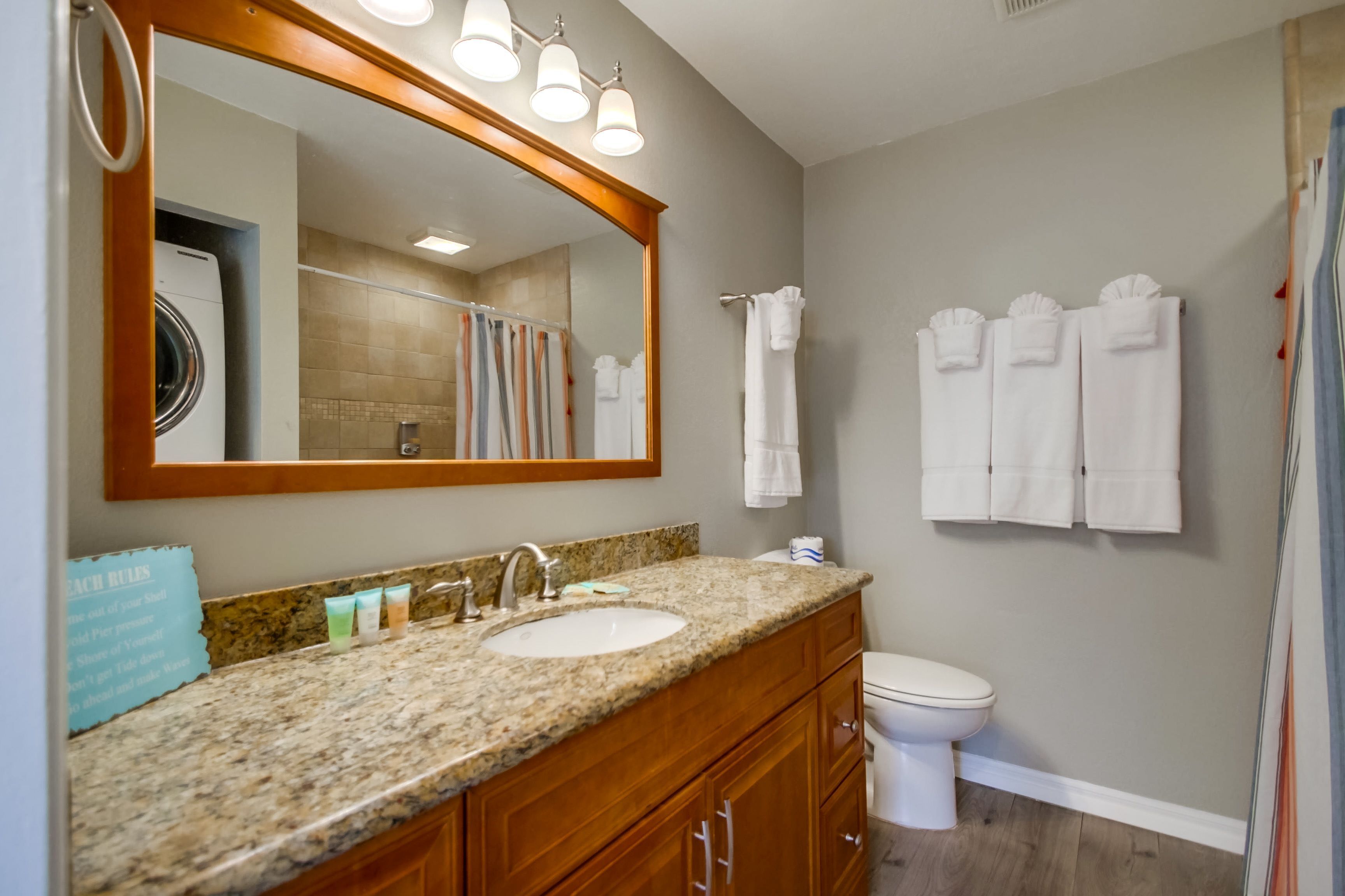 A bathroom with a granite countertop sink, wooden cabinets, a large mirror, and a toilet.