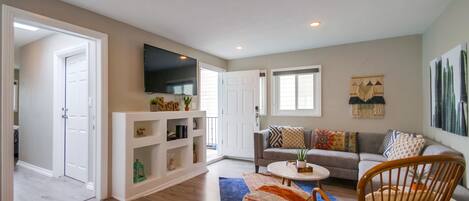 A spacious living room with a grey sofa, a white entertainment unit, and a large TV mounted on the wall.