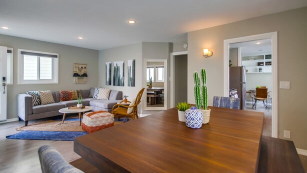 A modern living room with a wooden dining table, a gray sofa, and a kitchen visible through an open doorway. - Beautiful Apartment 5 minutes from the ocean (San Diego)