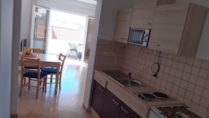 A kitchen with a microwave, sink, and stove. There is a dining area with chairs and a table.
