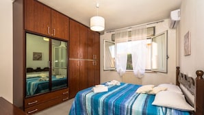 Un dormitorio con un armario grande de madera, una cama con colcha azul a rayas, una mesita de noche y una ventana con cortina.