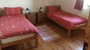 A bedroom with two single beds, wooden nightstands, and bedside lamps. - Groff Cottage (Tourmakeady)