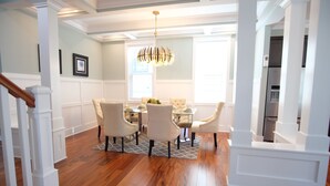 A dining area with a wooden floor, white walls, and a chandelier. There is a staircase on the left and a kitchen area on the right. - Luxury brand-new home mins away from Washington DC (Arlington)