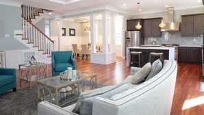 A spacious living area with a staircase, a dining area, and a kitchen with dark cabinets and pendant lighting. - Luxury brand-new home mins away from Washington DC (Arlington)