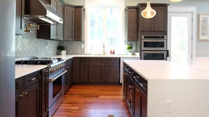 A modern kitchen with dark wood cabinets, stainless steel appliances, and a large island with a white countertop. - Luxury brand-new home mins away from Washington DC (Arlington)