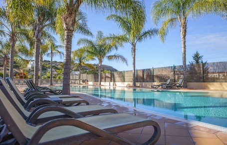 Una piscina al aire libre, sombrillas, sillones reclinables de piscina