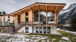Una casa moderna de fusta amb finestres grans i un balcó, envoltada de terra coberta de neu i muntanyes.