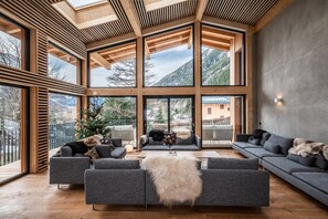 Un'ampia zona giorno con ampie finestre, travi in legno e vista sulle montagne.