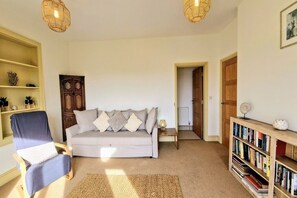 A cozy living room with a sofa, chair, bookshelf, and a door leading to another room.