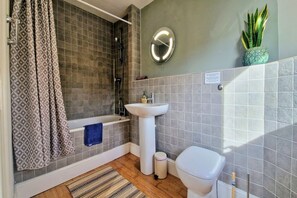 Et badeværelse med bruser, badekar, håndvask og toilet, samt en potteplante.