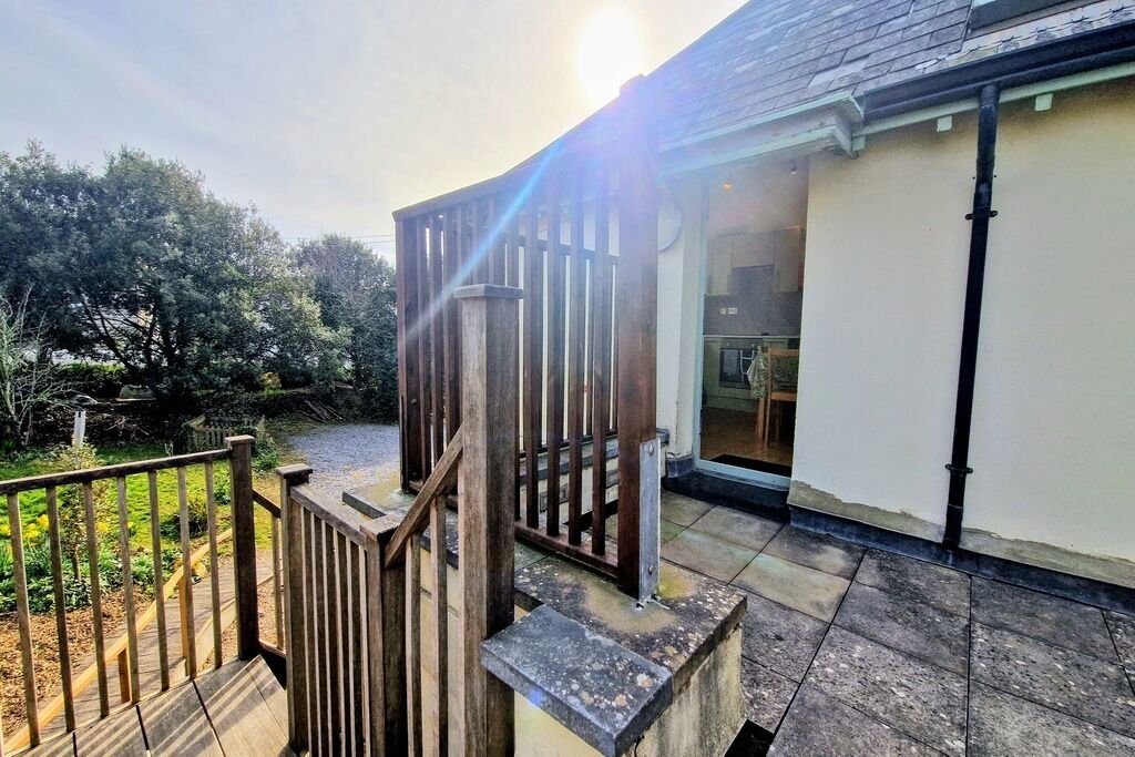A wooden staircase leading to a covered outdoor area with a view of a garden and trees.